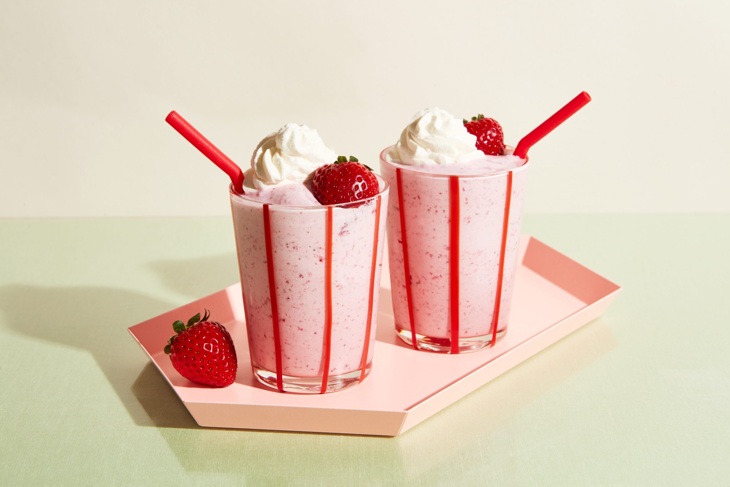  Strawberry barfi milkshake served in a tall glass, layered with creamy strawberry swirl, chunks of mithai-style barfi, and topped with rose petals and pistachio slivers