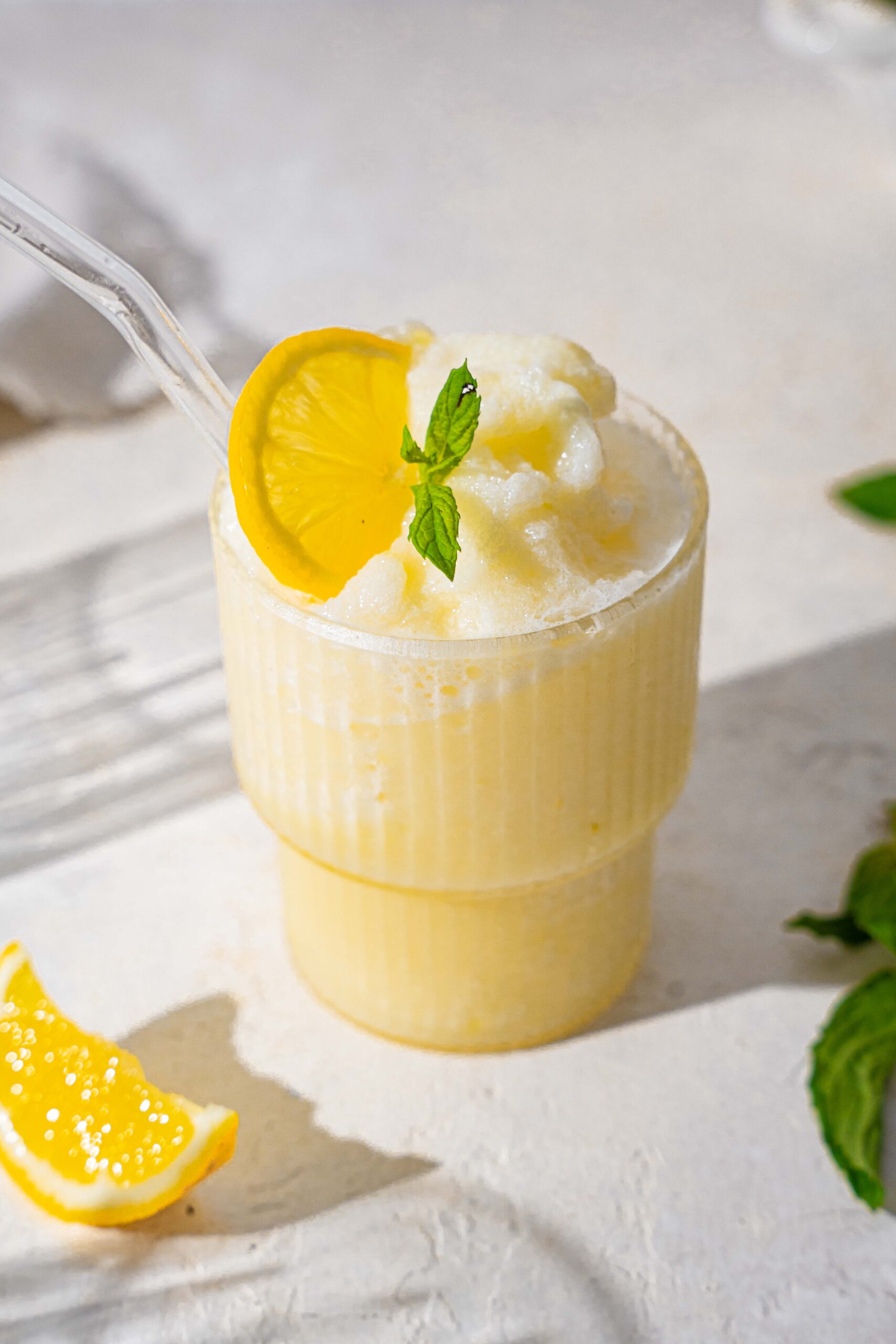 Glass with straw filled of drink garnished with cream and mint leaf and sliced lemon
